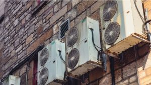 Multiple old, rusted air conditioning condenser units mounted on a wall, illustrating the need for A/C replacement due to age and inefficiency.