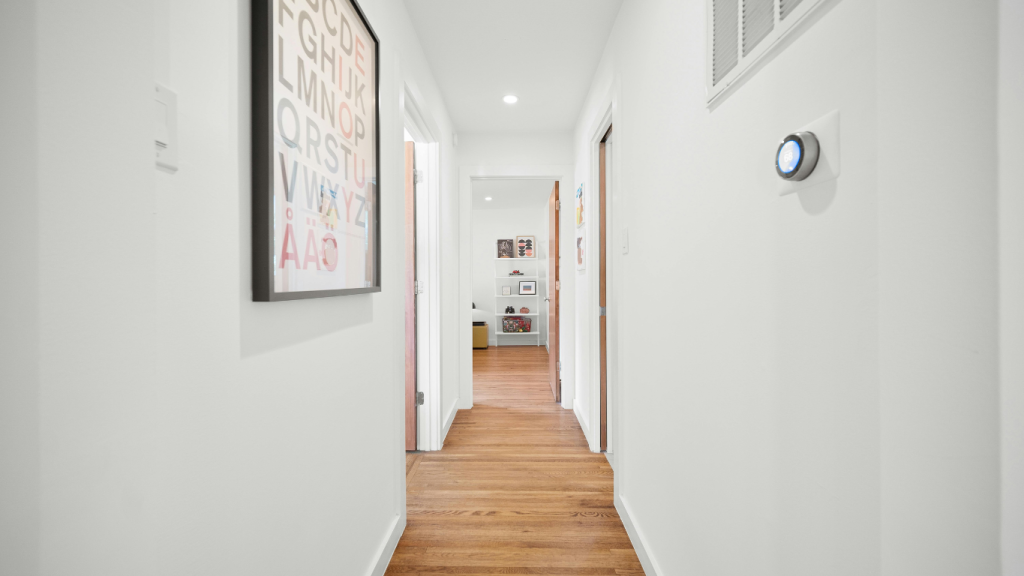 A modern smart thermostat installed in a hallway, used for air balancing and HVAC zoning to eliminate hot and cold spots.