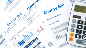 A calculator next to high electric bills and energy usage charts, illustrating the cost of an inefficient air conditioning system.