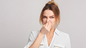A woman pinching her nose with a look of disgust, representing the homeowner's negative reaction to a foul, musty odor coming from their A/C unit.