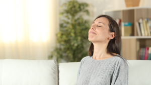 A happy, relaxed mom sitting on a couch and breathing in deeply, enjoying the fresh, clean indoor air quality in her home after an A/C service.