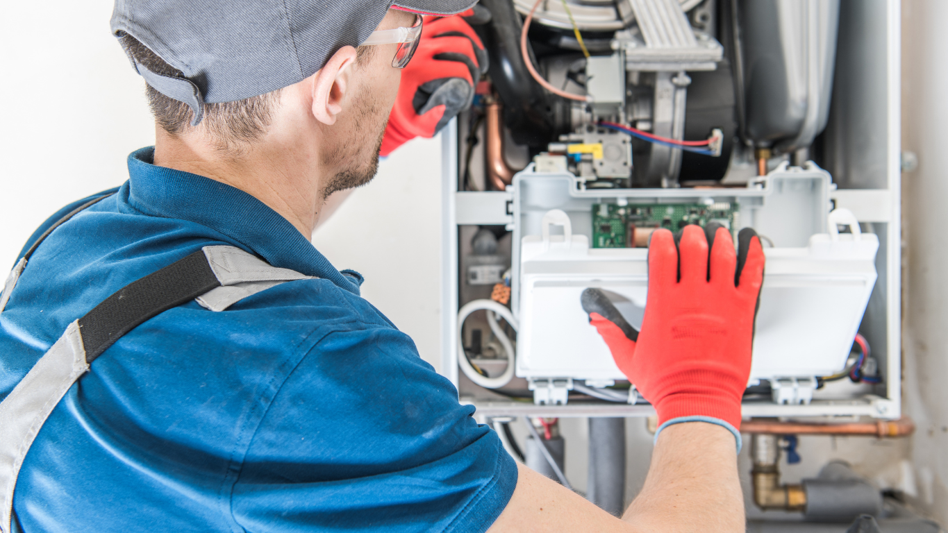 A certified HVAC technician in uniform and gloves performing a repair on a furnace, checking the internal components and wiring.