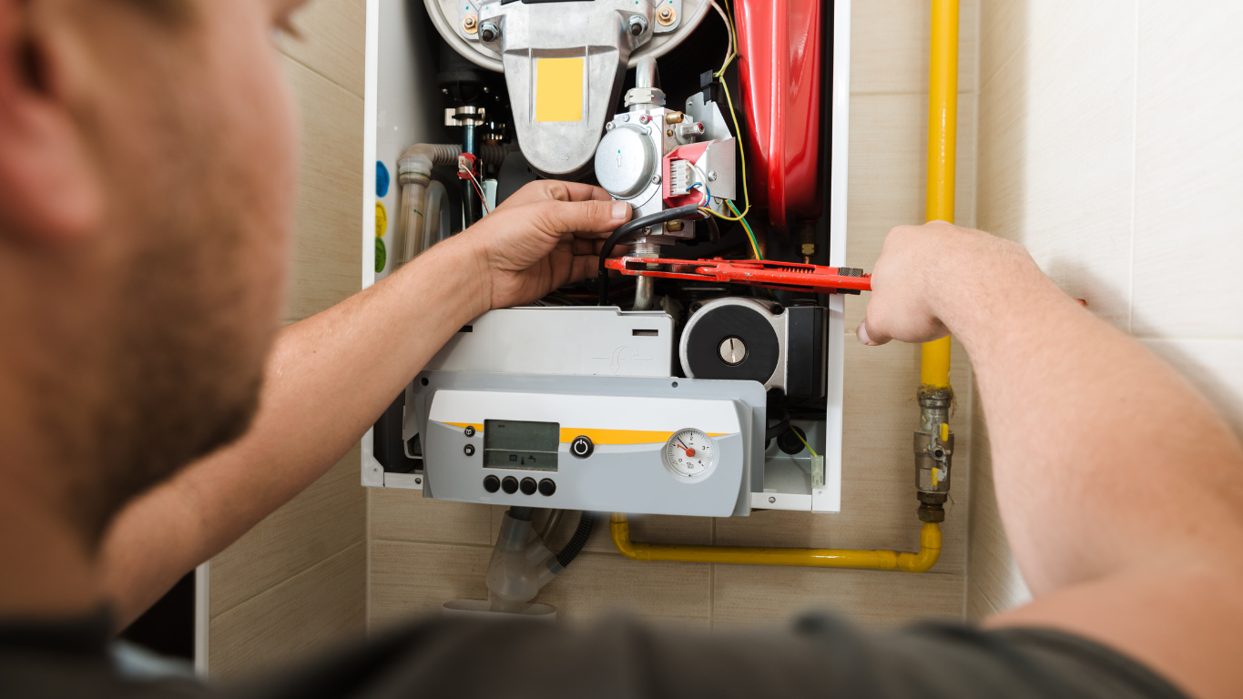 A close-up, over-the-shoulder view of a heating technician using a wrench to service a modern, wall-mounted gas furnace with a digital display.